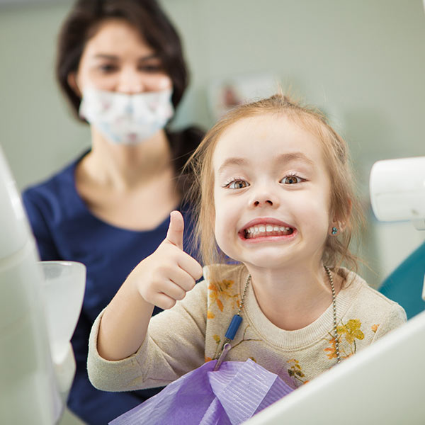 little girl giving thumbs up at dentist office